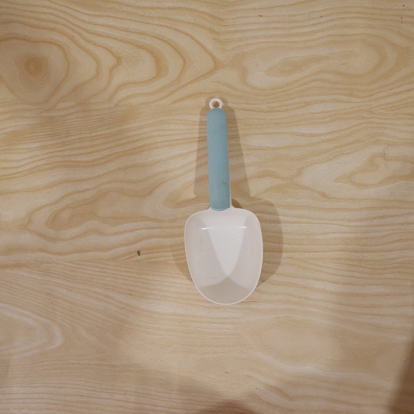A white plastic measuring spoon demonstrating its use as a bag clip on a food bag.