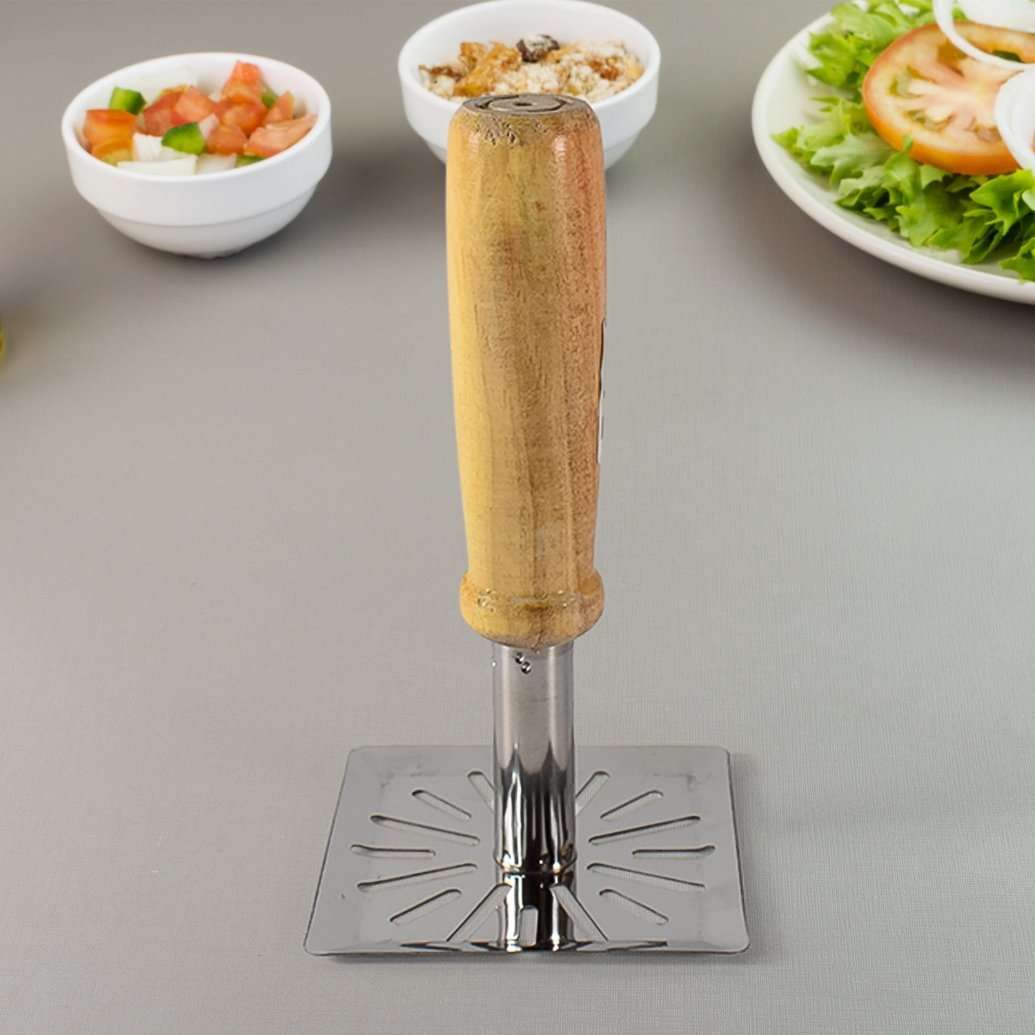 Stainless steel potato masher with wooden handle on a kitchen surface