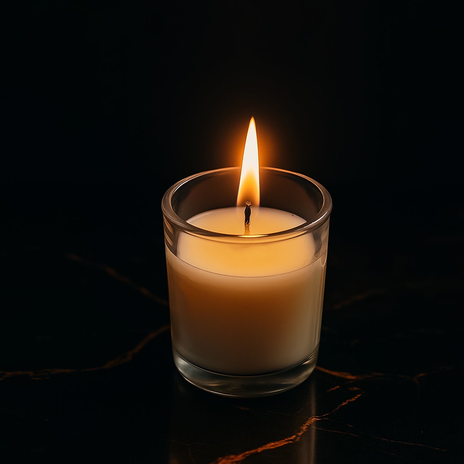 A lit Scented Votive Candle in a clear glass jar, casting a warm glow.