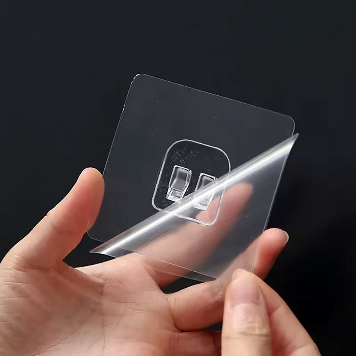 Transparent self-adhesive wall hook seamlessly mounted on a clear glass surface.