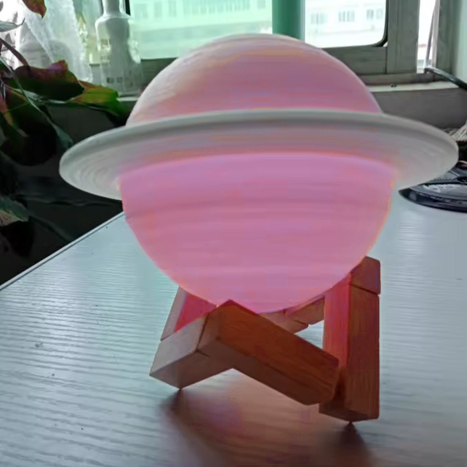 The 3D Saturn lamp presented with its power cable and wooden stand.
