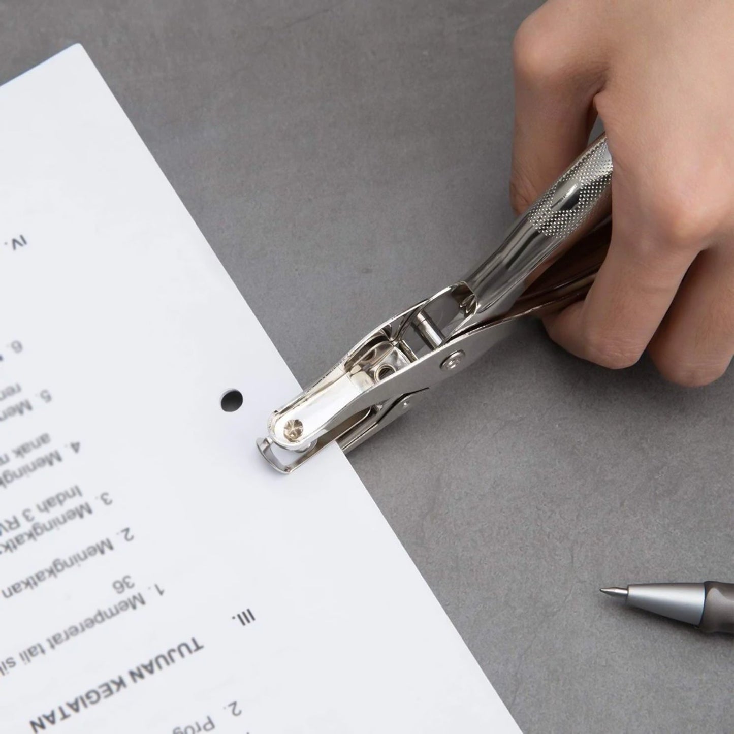 Handheld metal hole puncher in action, cleanly punching through paper.