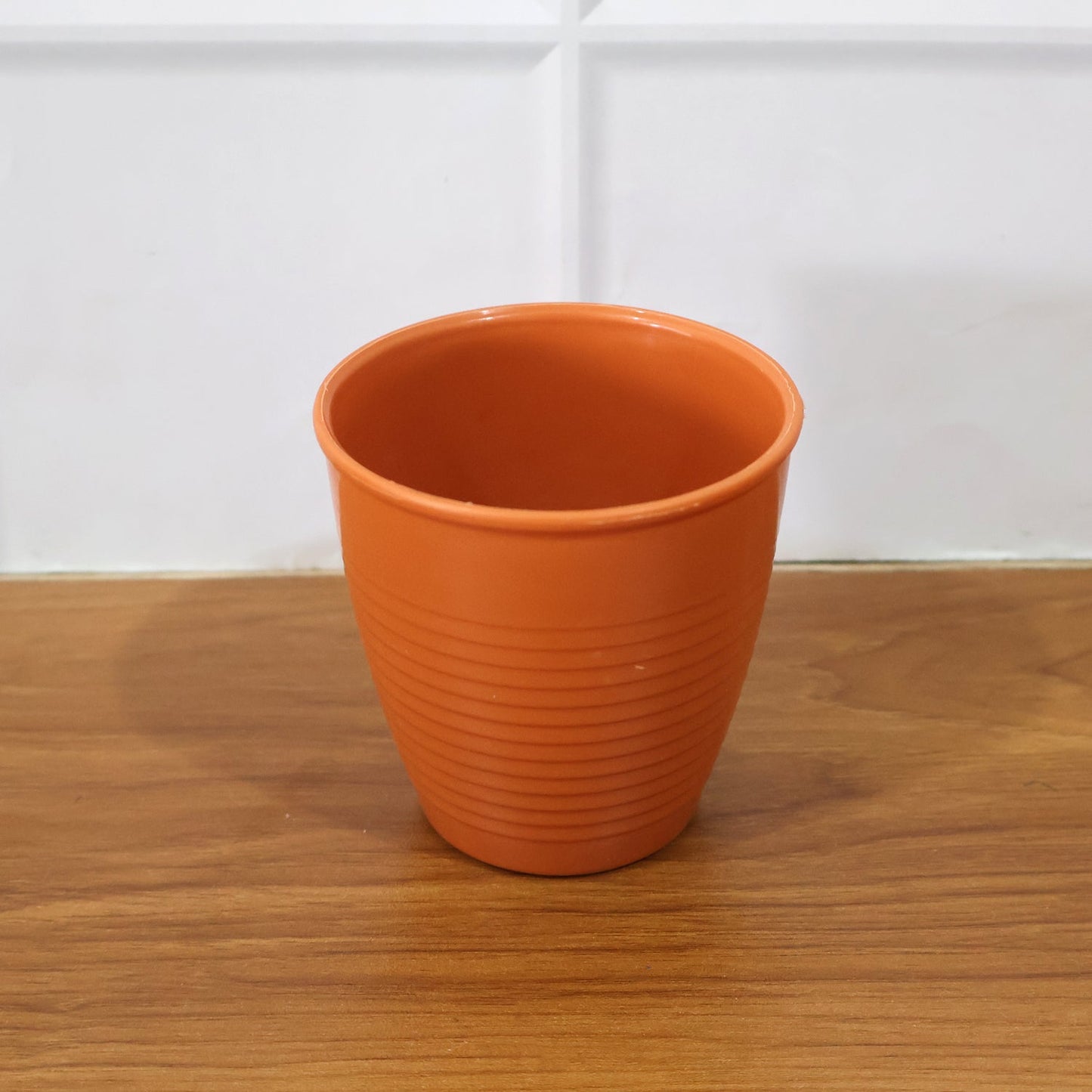Angled view of plastic small drinking glass with tapered body on white background