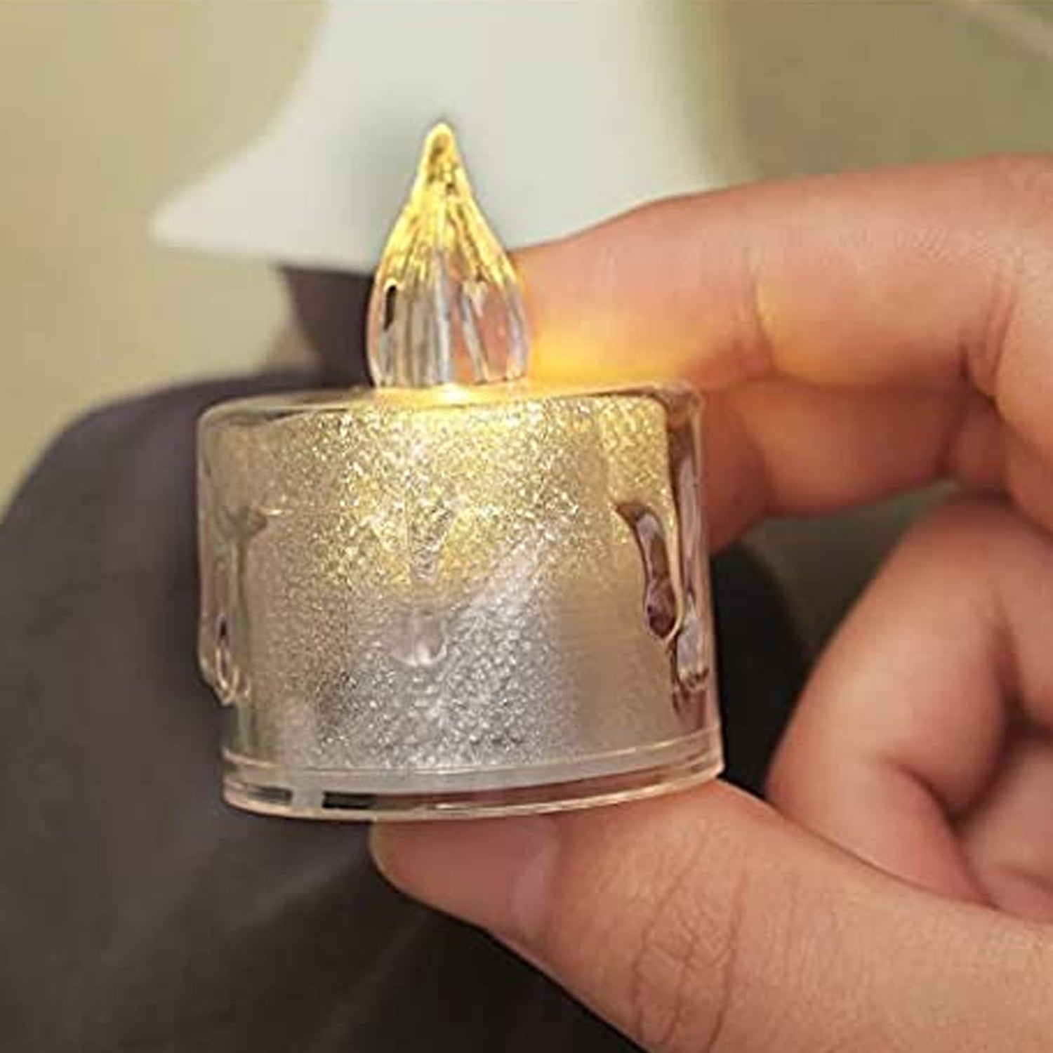 A hand gently holding a single transparent flameless LED tea light candle.