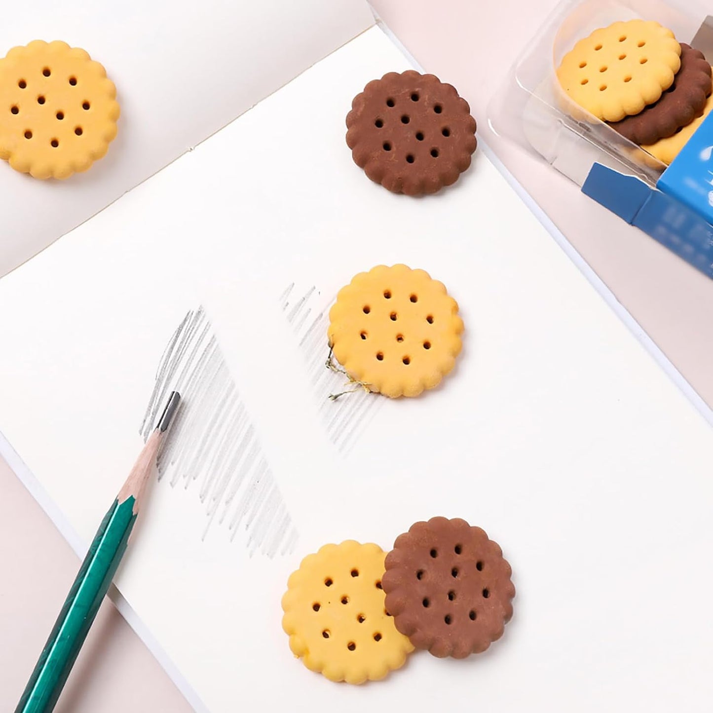 A child's hand holding a fun biscuit eraser next to a pencil, showing usage.
