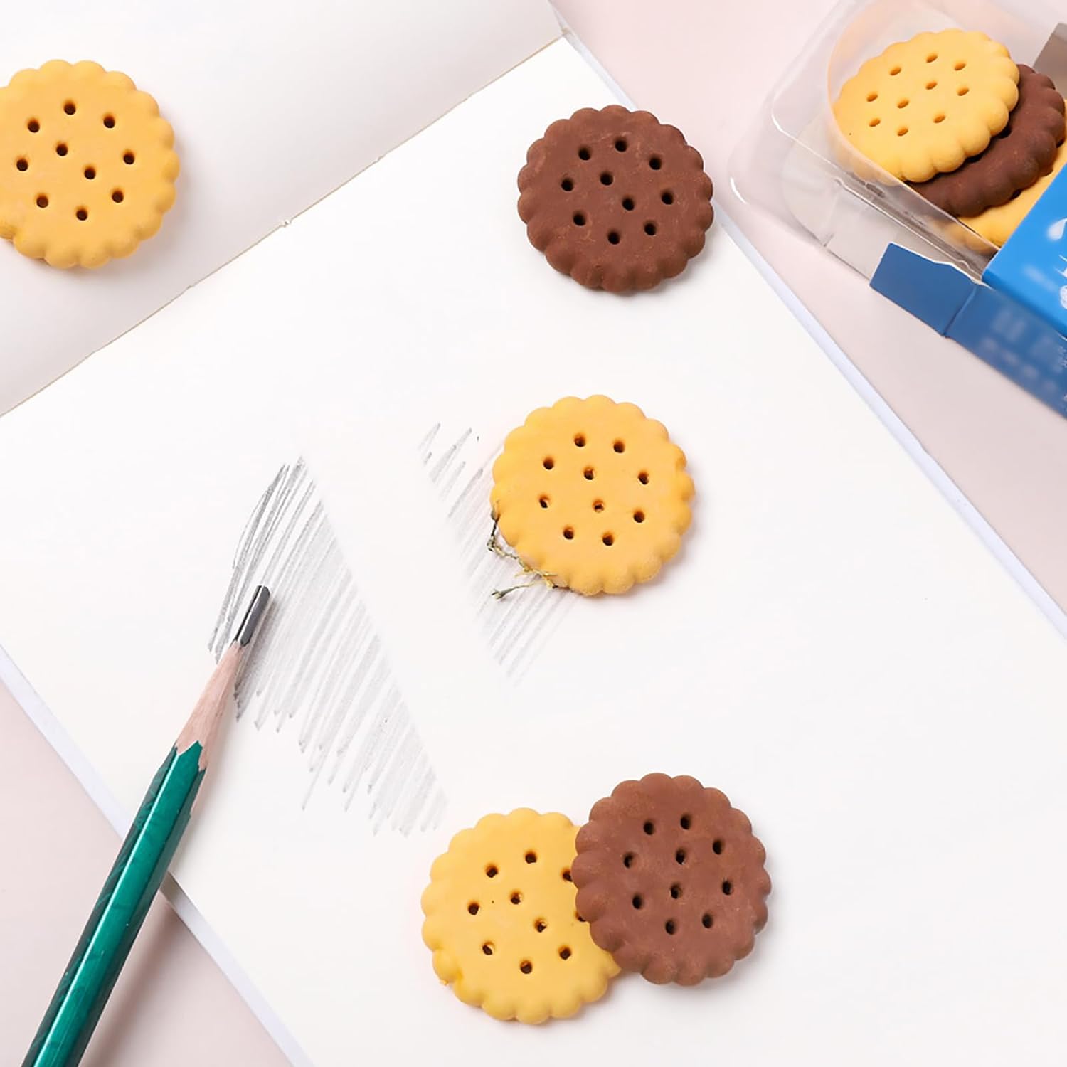 A child's hand holding a fun biscuit eraser next to a pencil, showing usage.