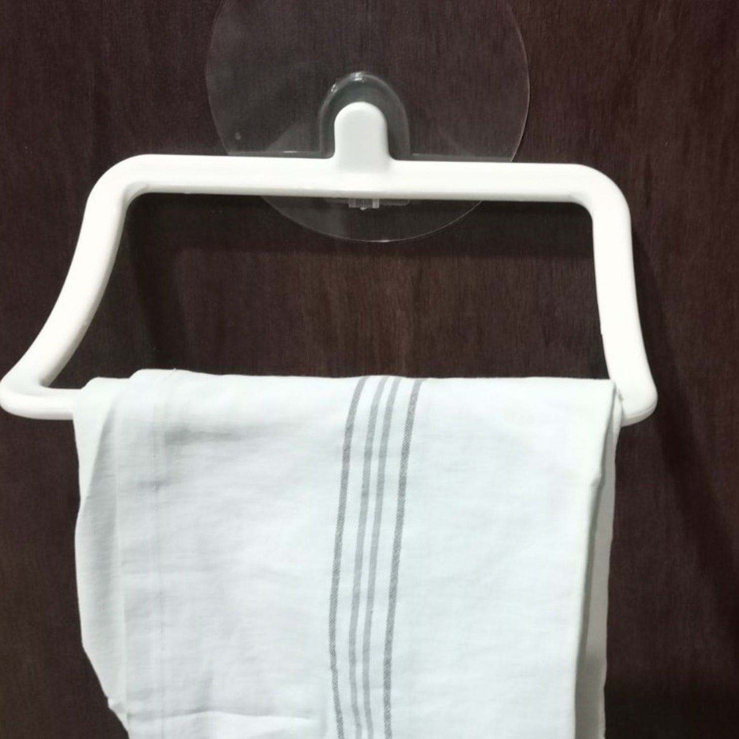 A sleek self-adhesive towel holder mounted on a tiled bathroom wall, holding a white hand towel.