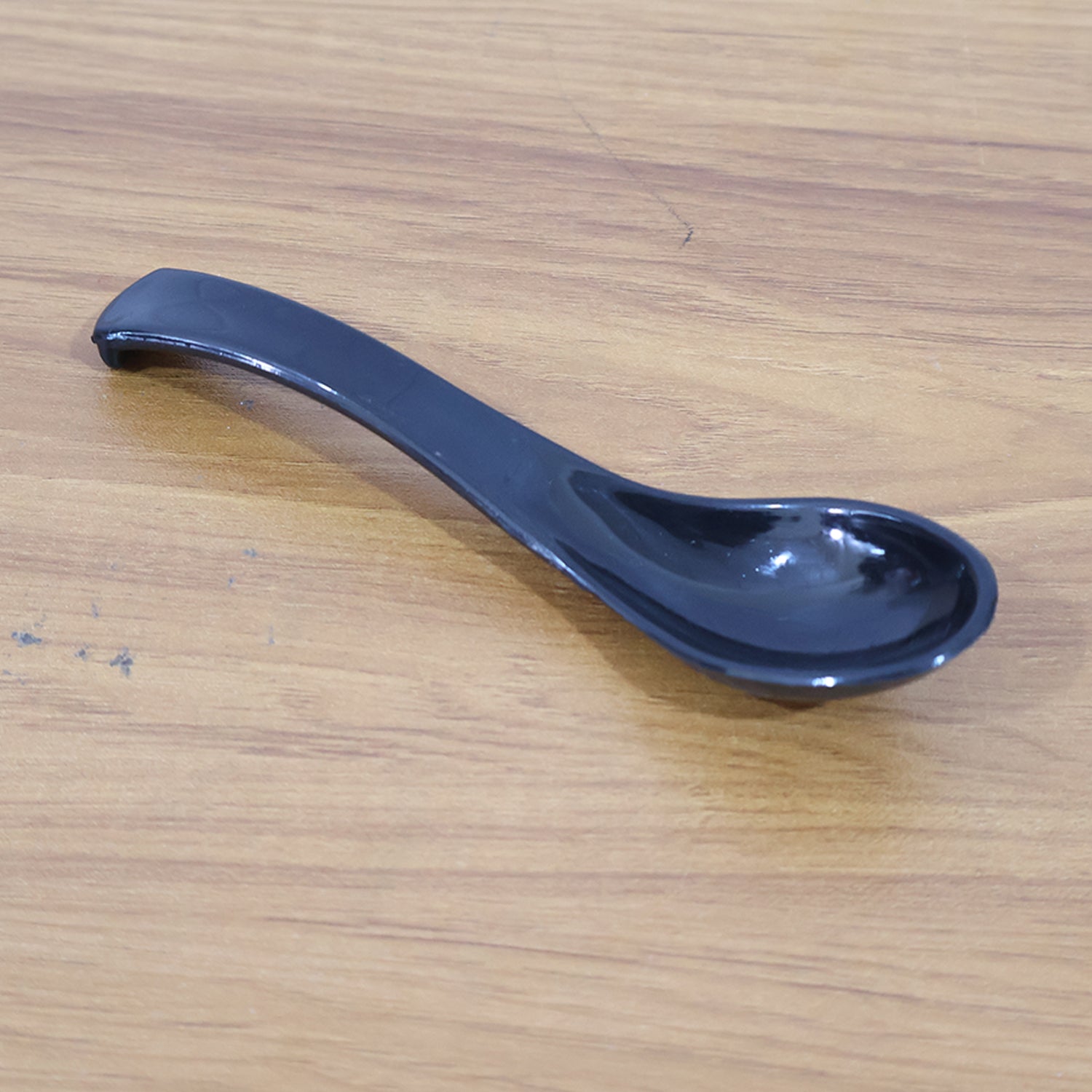 Angled view of black plastic soup spoon with deep bowl and ergonomic handle